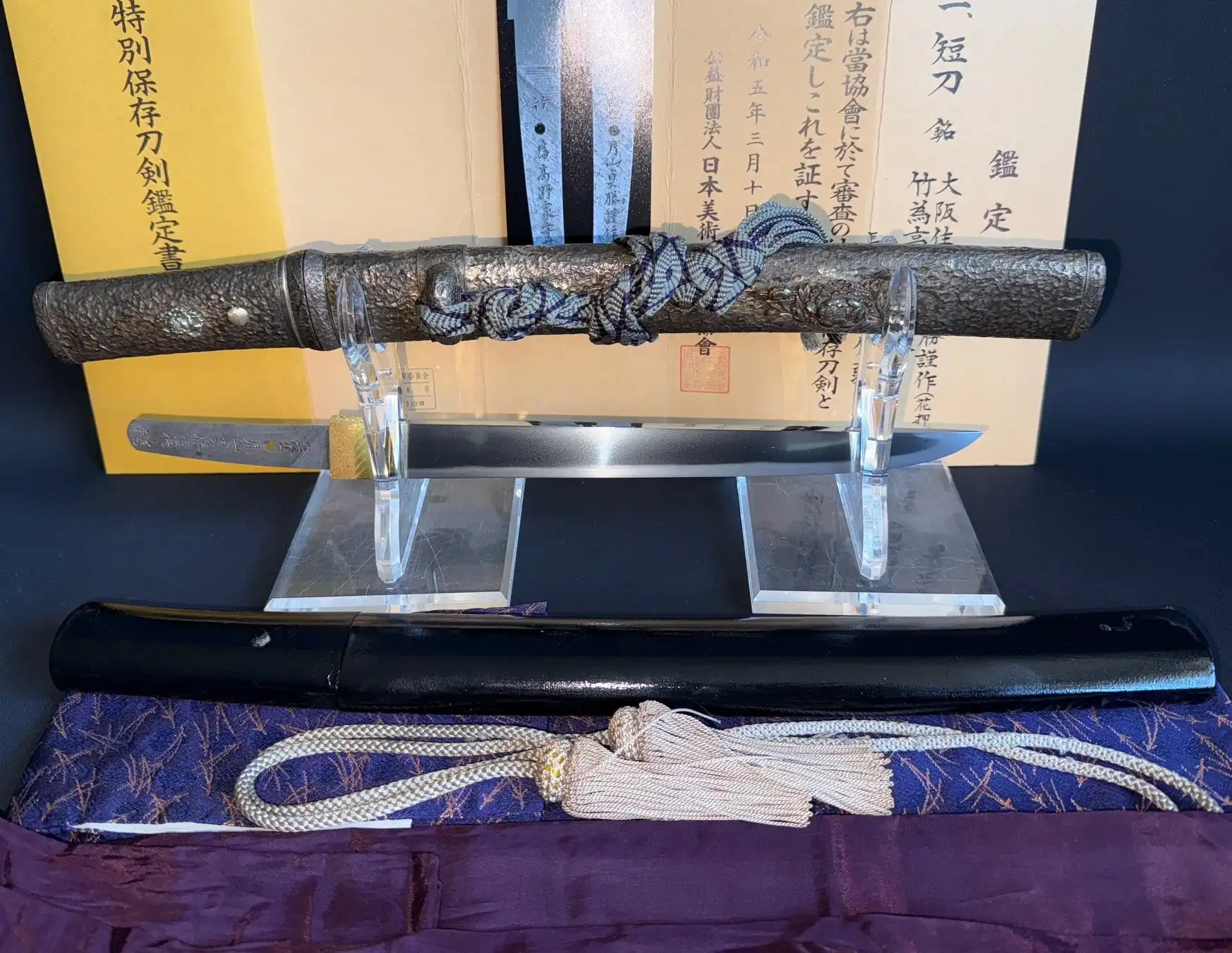Tanto Gassan Sadakatsu on display by Kyodai Originals, with saya, cord, and Japanese papers visible