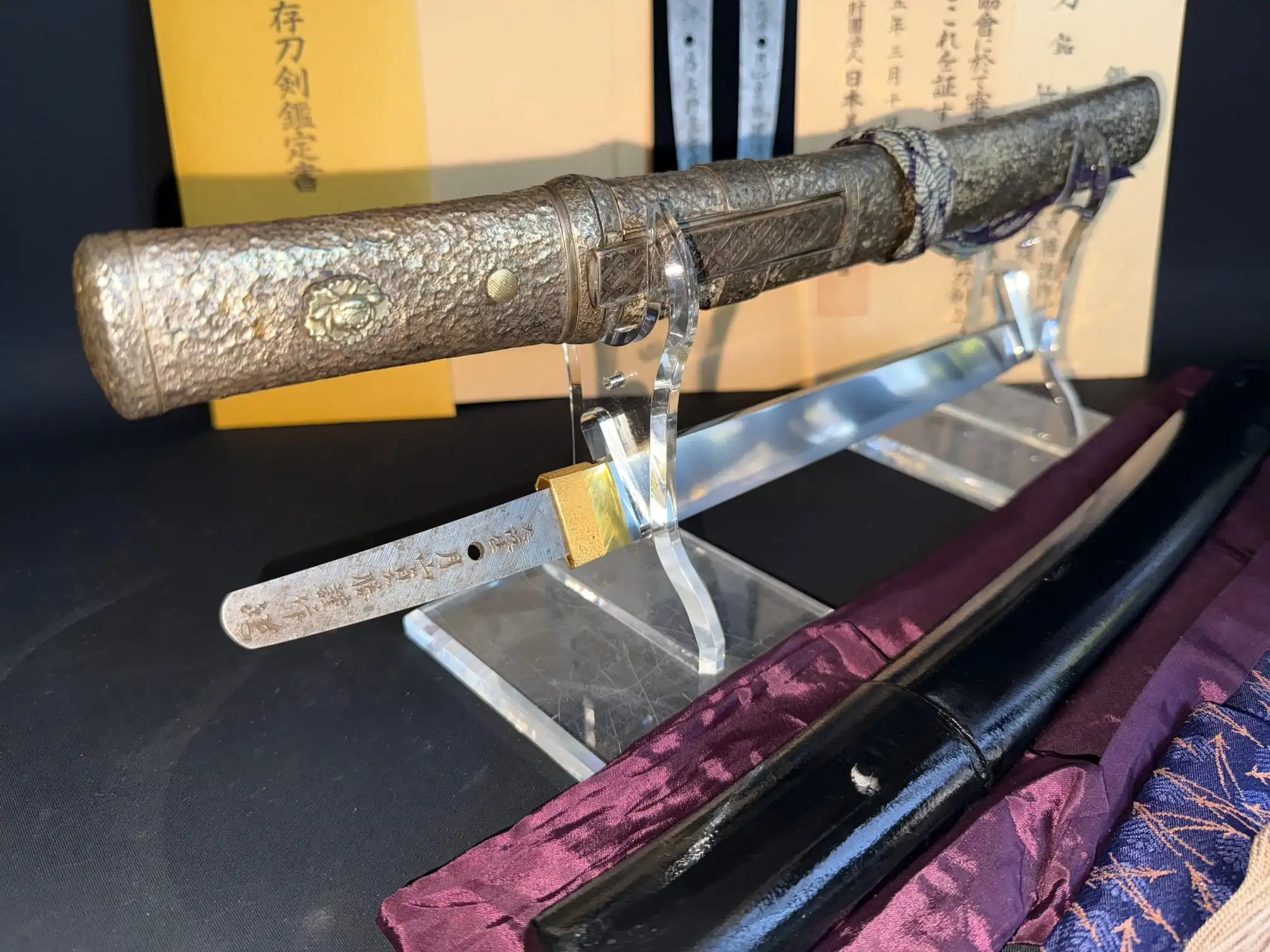 Tanto Gassan Sadakatsu, an antique Japanese short sword on a stand with its scabbard, gold fittings visible