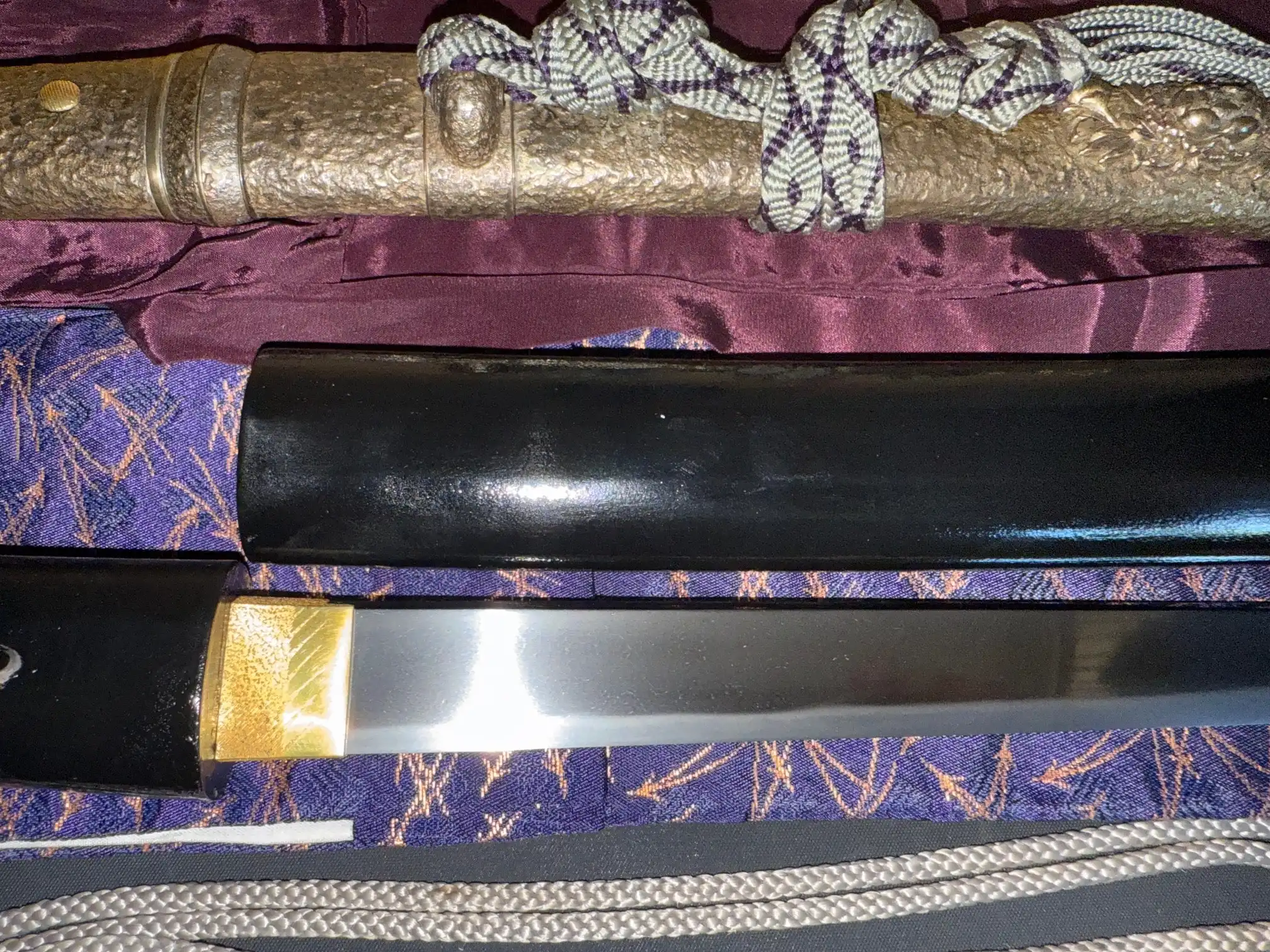 Kyodai Originals Tanto Gassan Sadakatsu, shiny blade emerging from black saya, with golden habaki and wrapped tsuka.