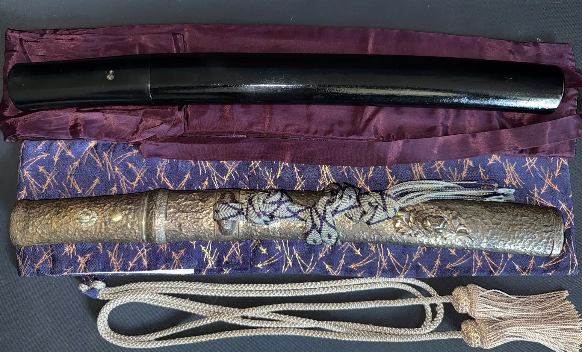 Gassan Sadakatsu Tanto hilt with ornate metalwork and cord, black lacquer saya above, on purple fabrics