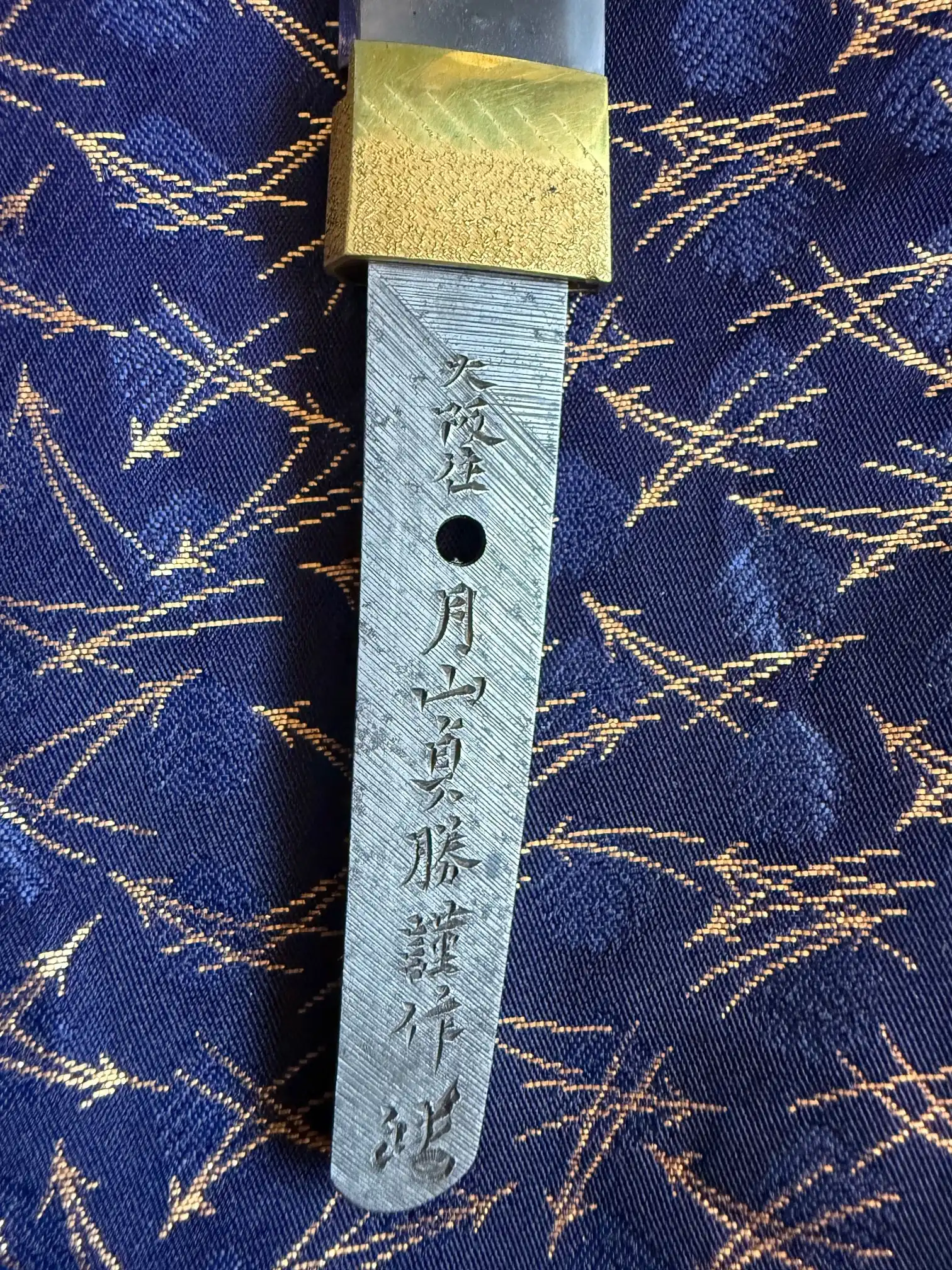 Tanto Gassan Sadakatsu nakago (tang) with chiselled signature and gold habaki on blue fabric.