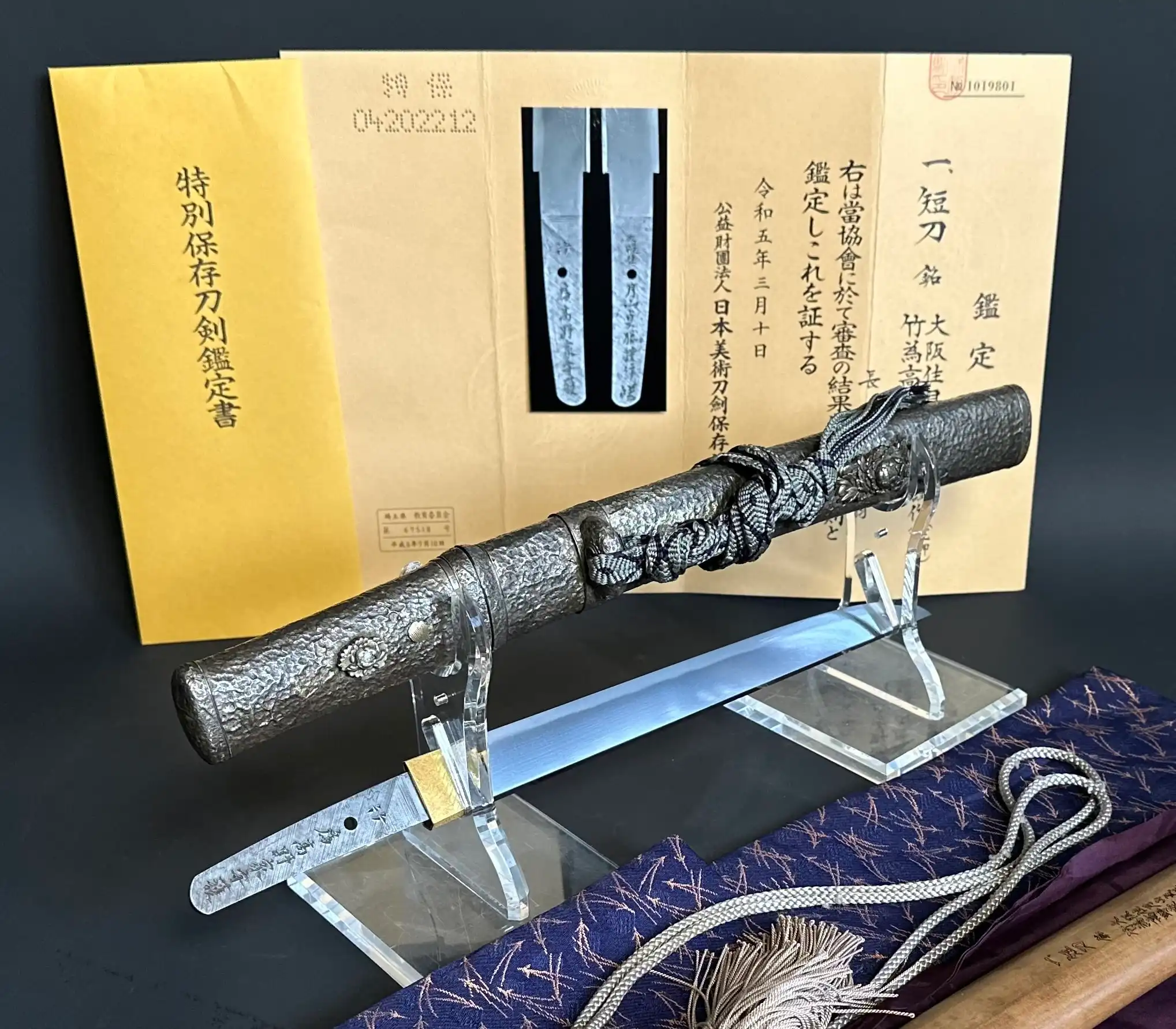 Tanto Gassan Sadakatsu, an antique Japanese short sword on a stand with its scabbard, NBTHK paper behind