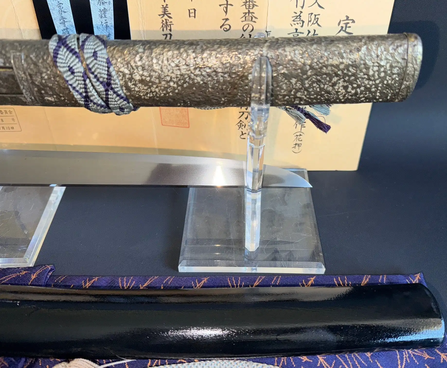 Polished Tanto Gassan Sadakatsu blade next to its textured samegawa tsuka and black lacquer saya on display