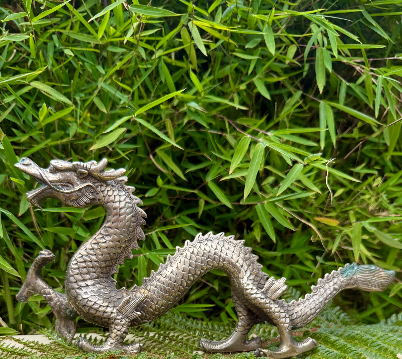 Silvered japanese dragon sculpture katana, Meiji Period style, detailed scales, against green bamboo foliage