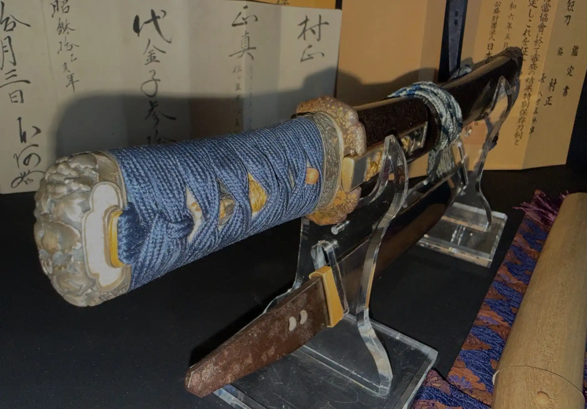 Tantō Muramasa Demon Steel with blue tsuka-ito on display, historical papers in background