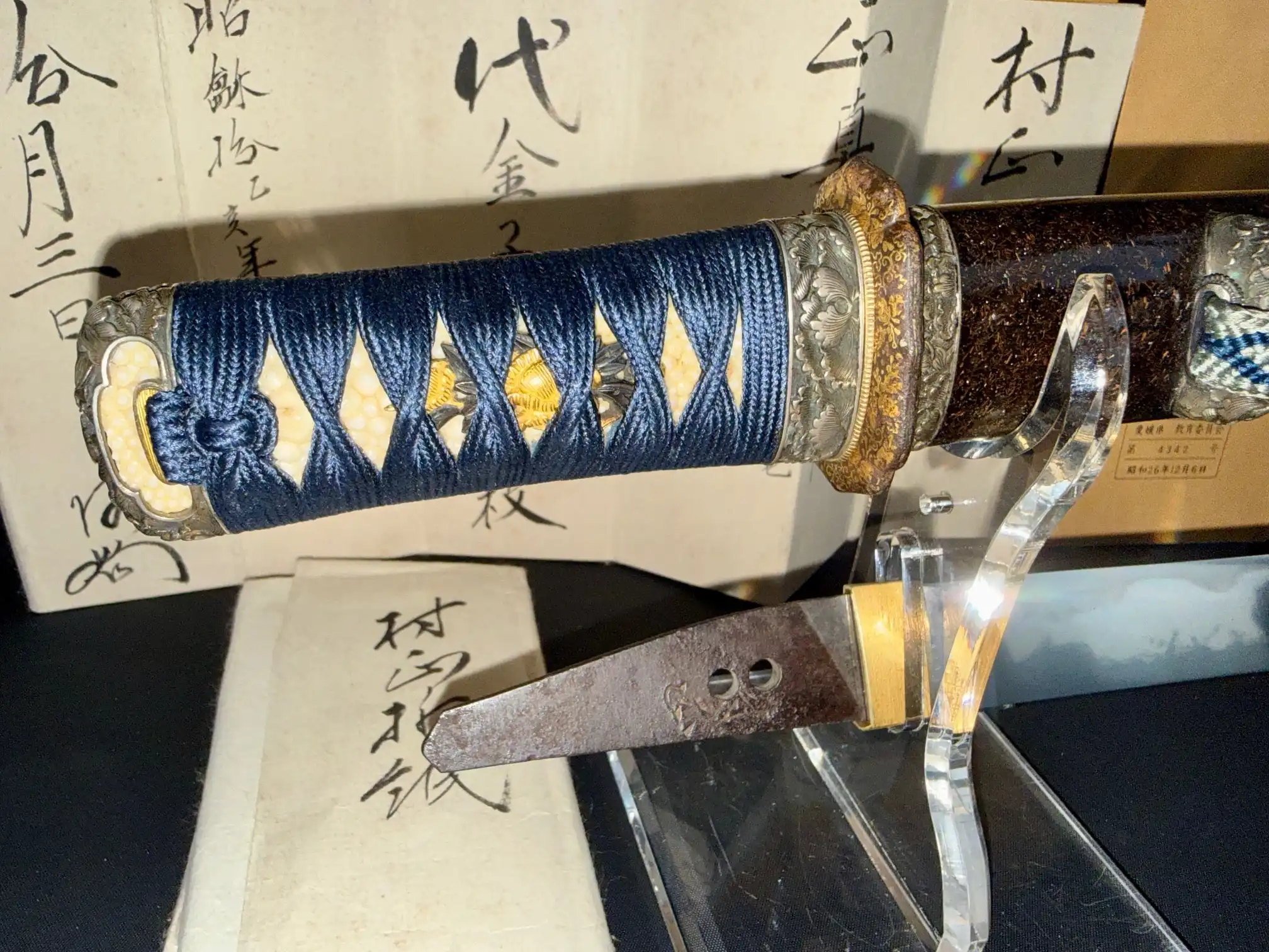 Tantō Muramasa Demon Steel with blue tsuka-ito, ornate fuchi, and visible nakago, on display