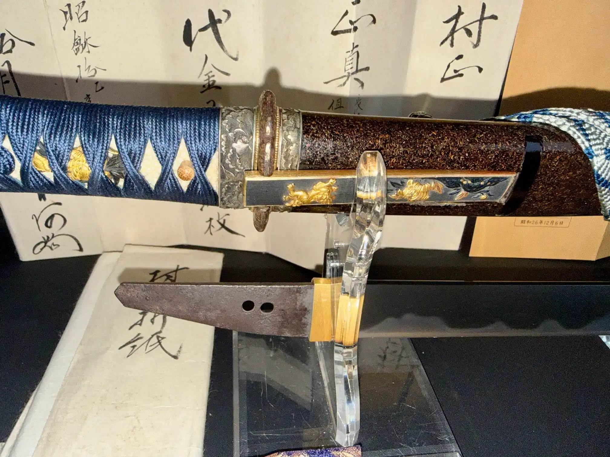 Close-up of a Tantō Muramasa Demon Steel blade with rust patination on display, handle, and scabbard