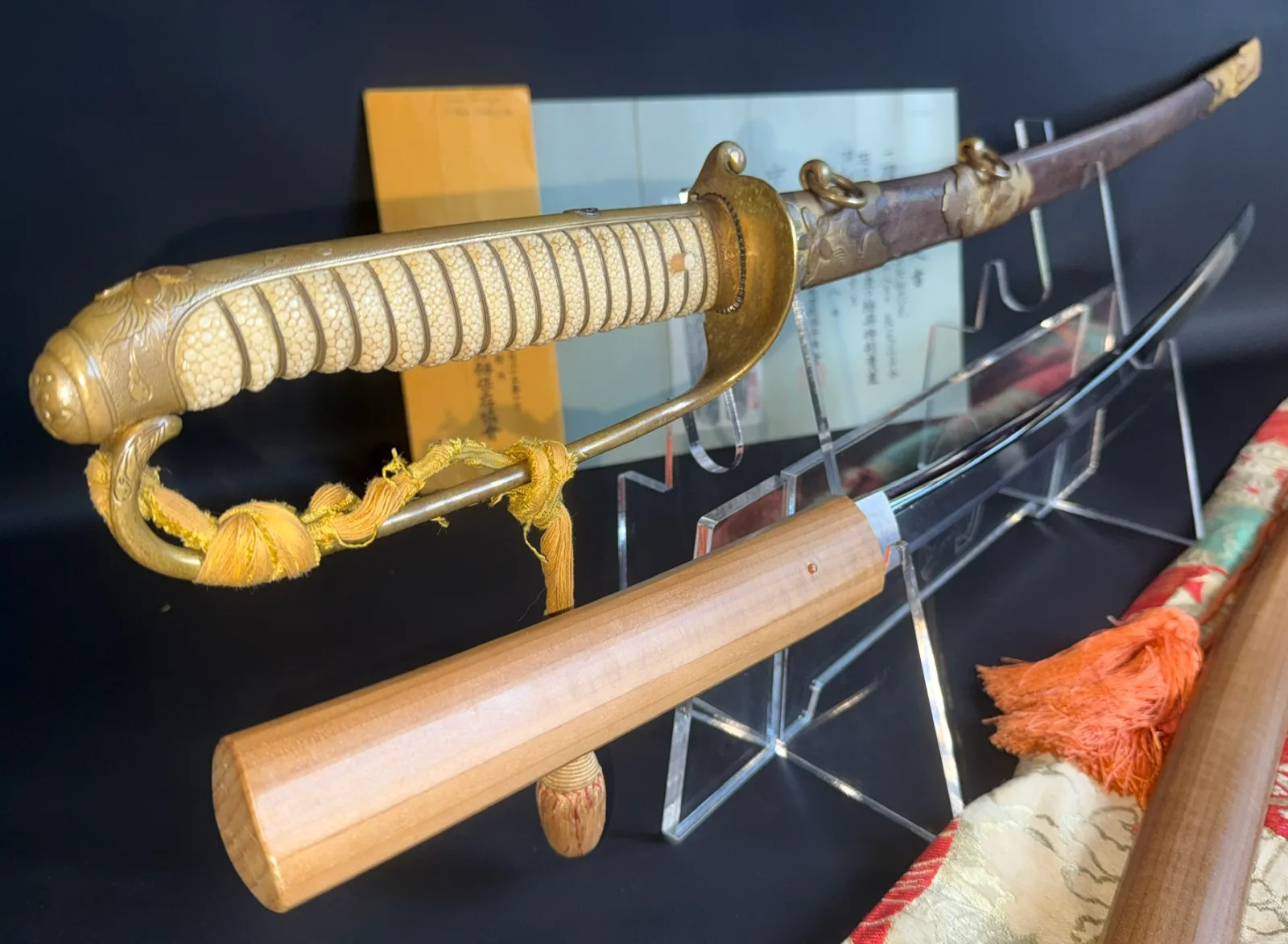 Naruse Family Heirloom katana with Naval Kyū Guntō koshirae, gold handle, and uncovered blade on a display stand.