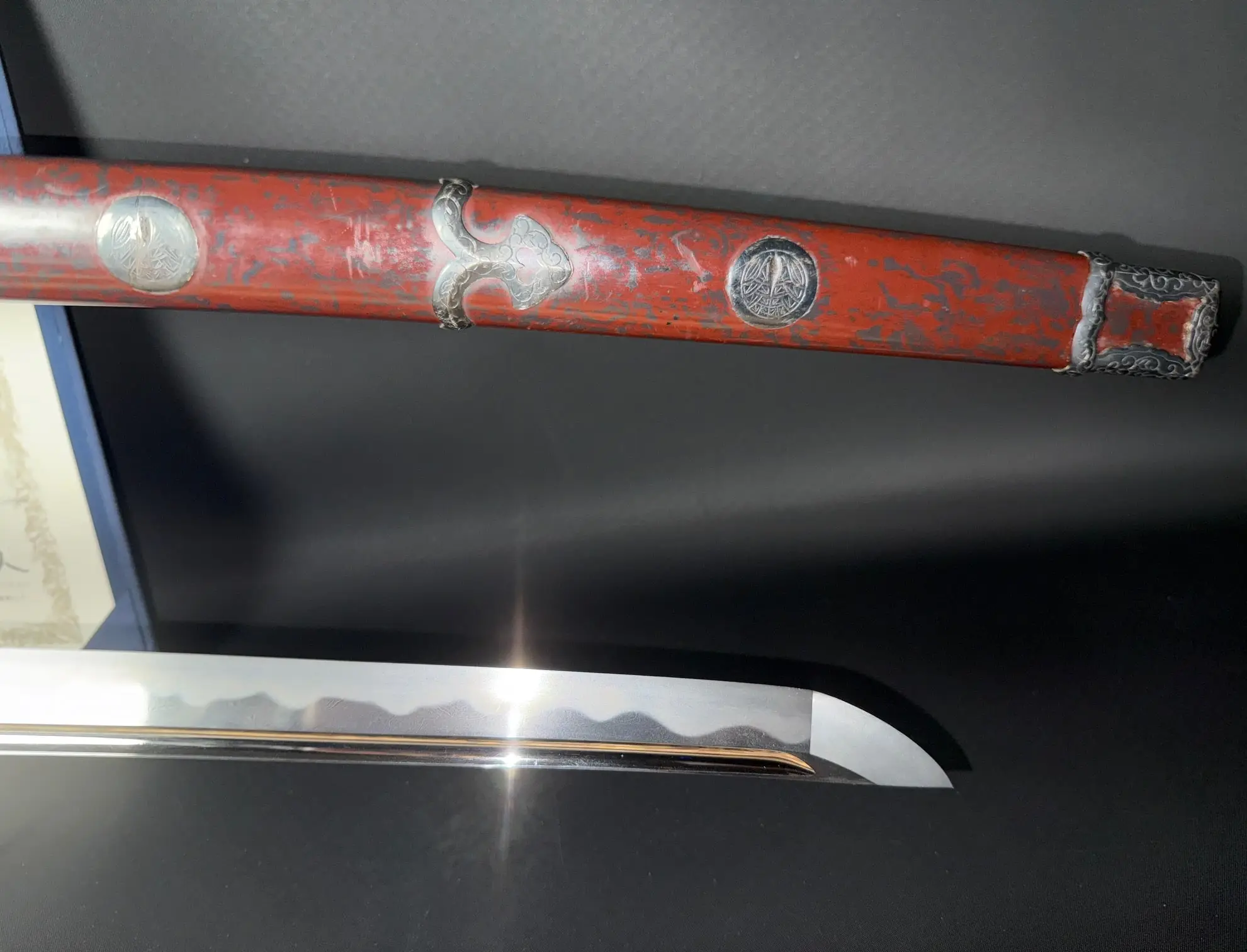 Tachi Katana Sadayoshi/Sadahito sword close-up, showing red saya and blade with hamon reflecting light.