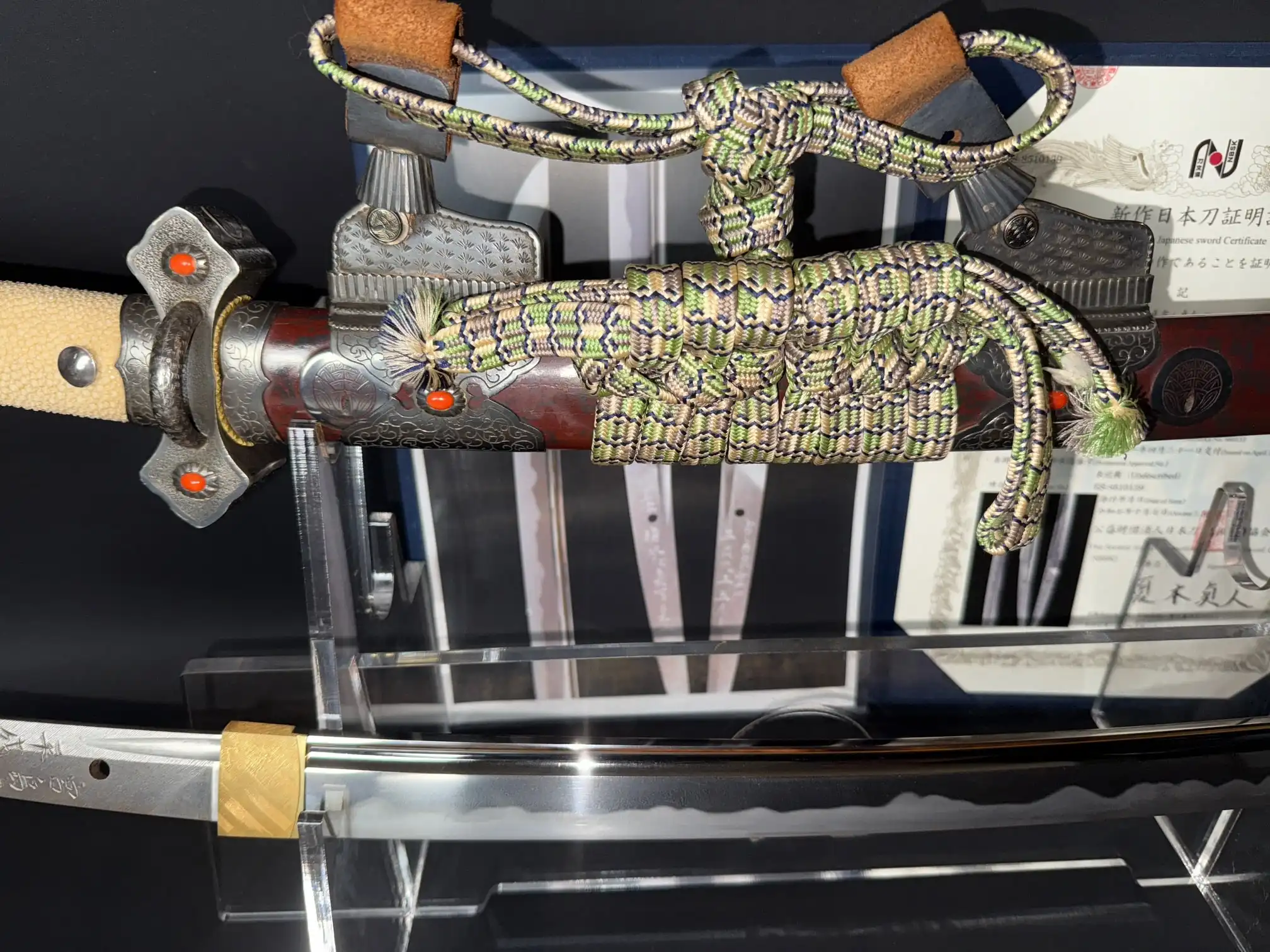 Side view of a Tachi Katana Sadayoshi/Sadahito, showing a collaborative Katana sword with ornate hilt and braided cord.
