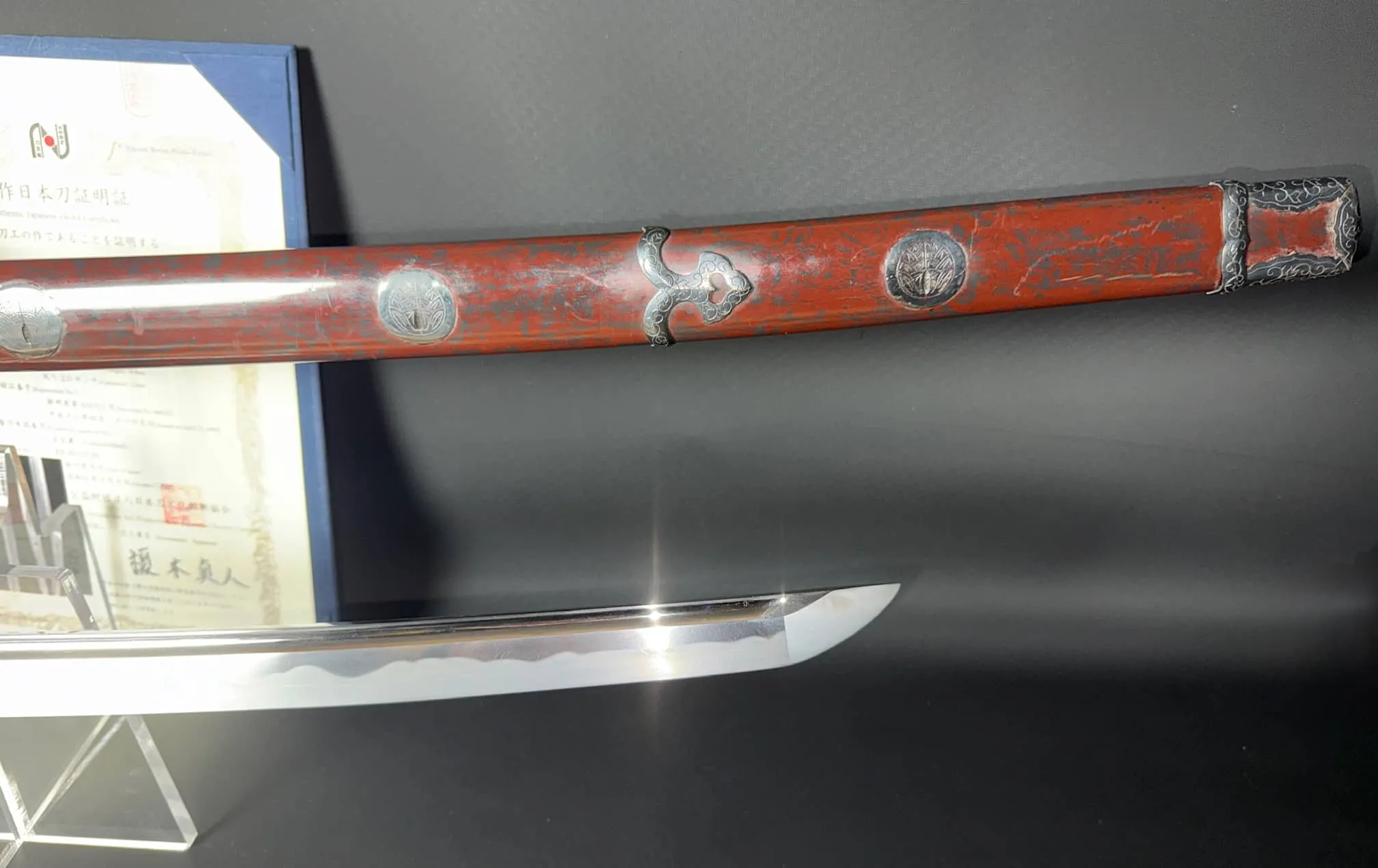 Tachi Katana Sadayoshi/Sadahito, a Katana in a red saya with silver accents, beside its gleaming blade.