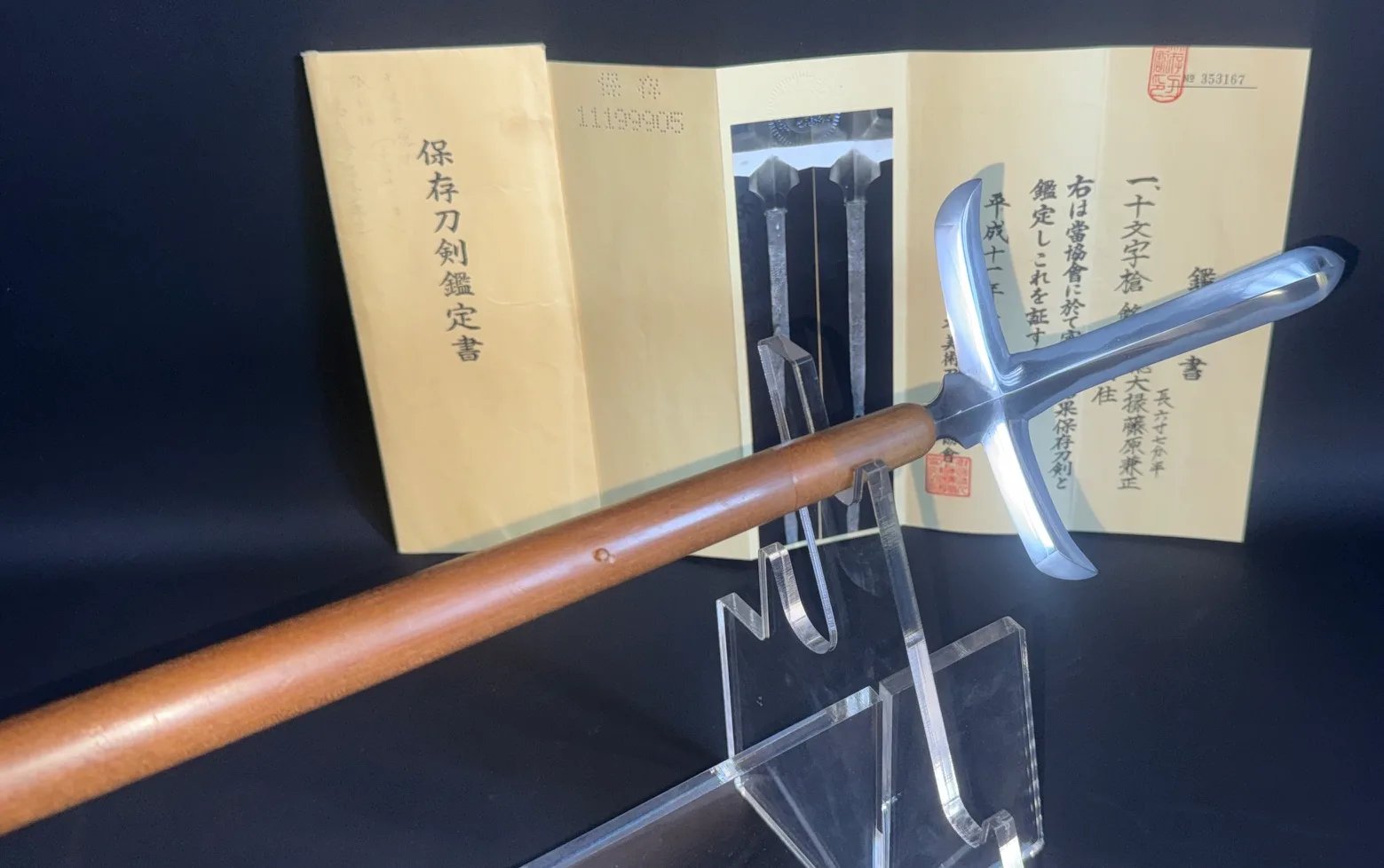 Rare Ichimonji-Yari on display stand, its cross-shaped blade shining, NBTHK Hozon certificate visible in background.